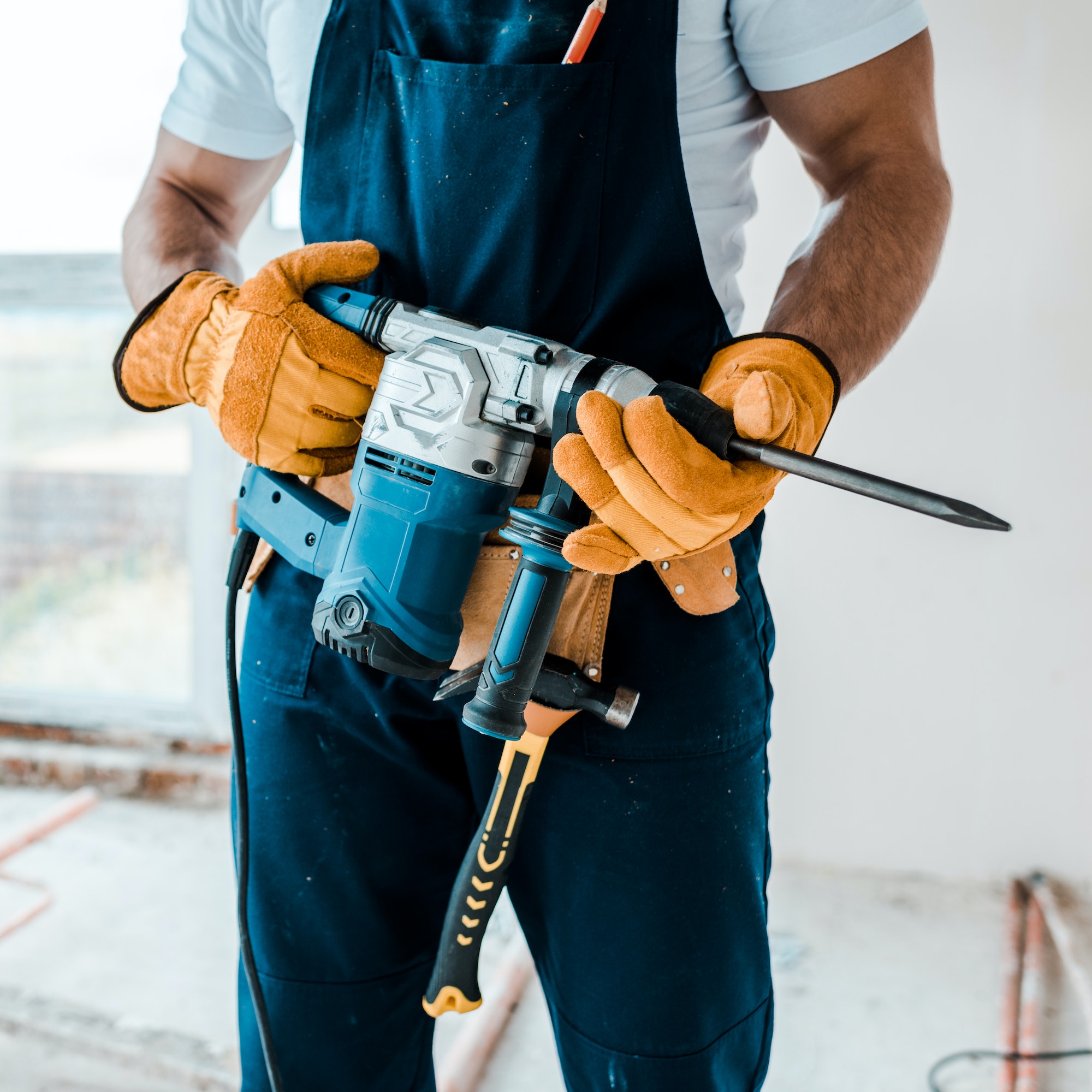 cropped view of workman in uniform and yellow gloves holding hammer drill